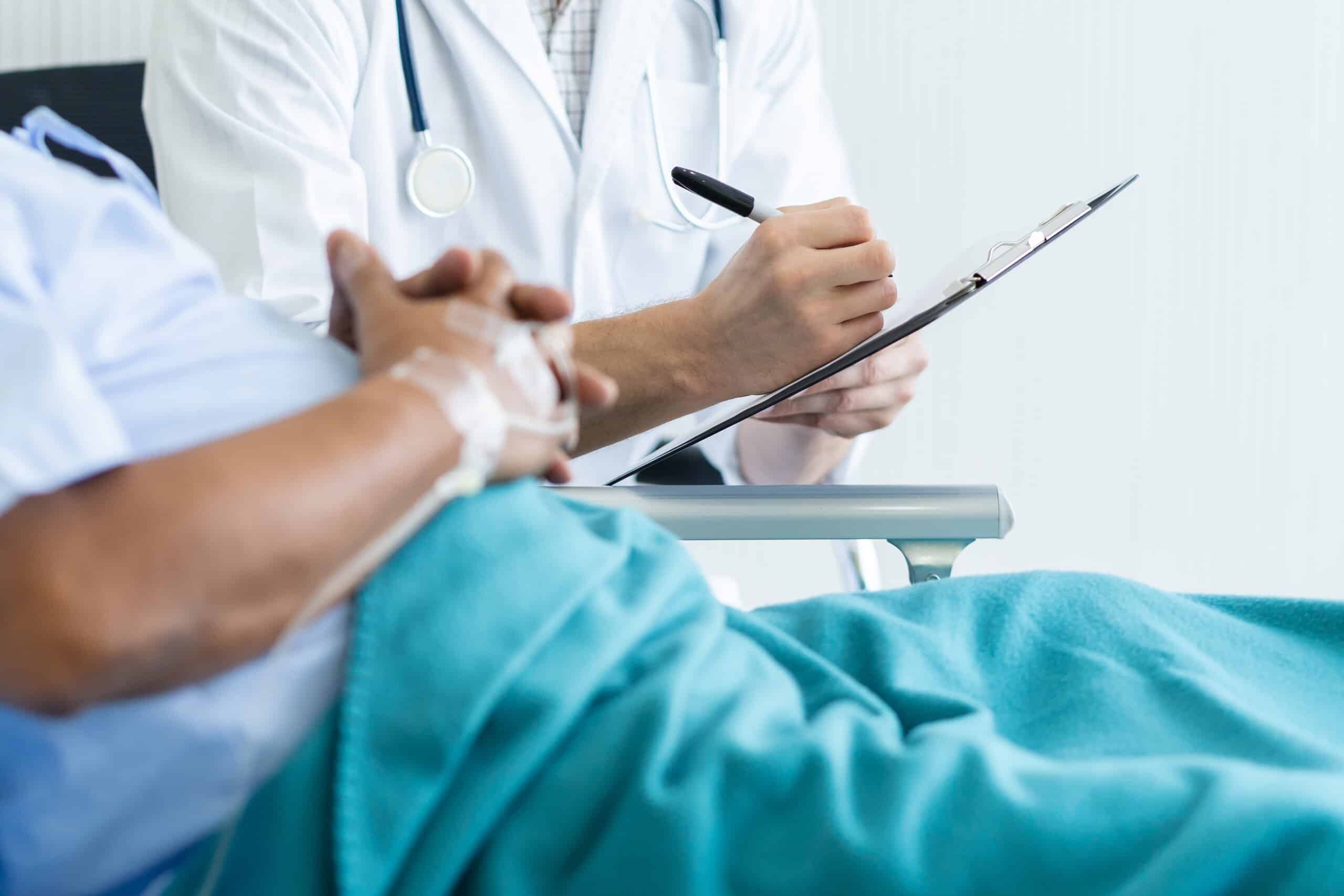 Doctor writing medical notes on a clipboard beside a seated patient.