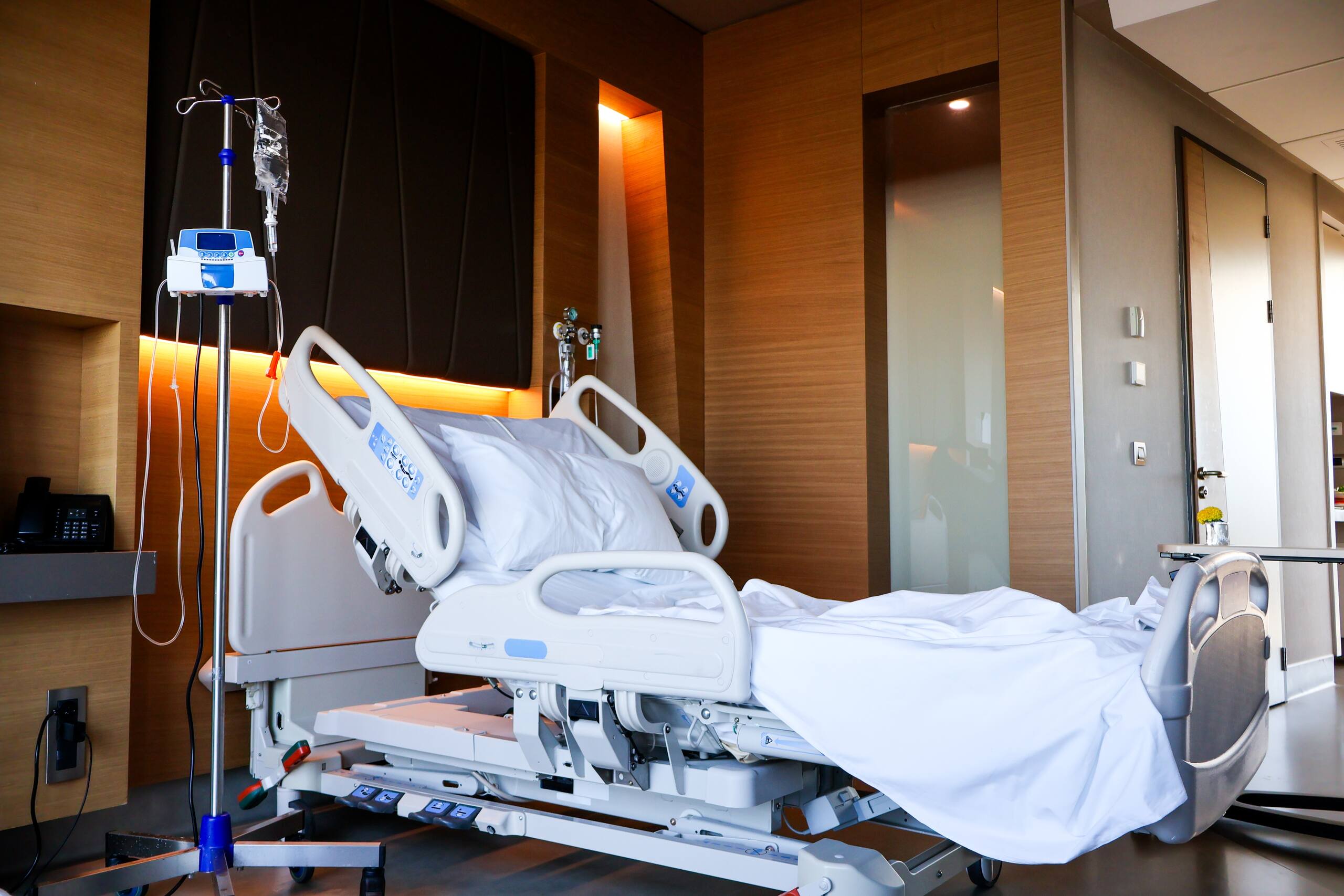 Empty hospital bed with an IV drip pole in a private medical room.