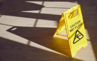 A yellow caution wet floor sign standing on a wooden floor with long shadows, representing an open and obvious hazard in a Scranton slip and fall case.
