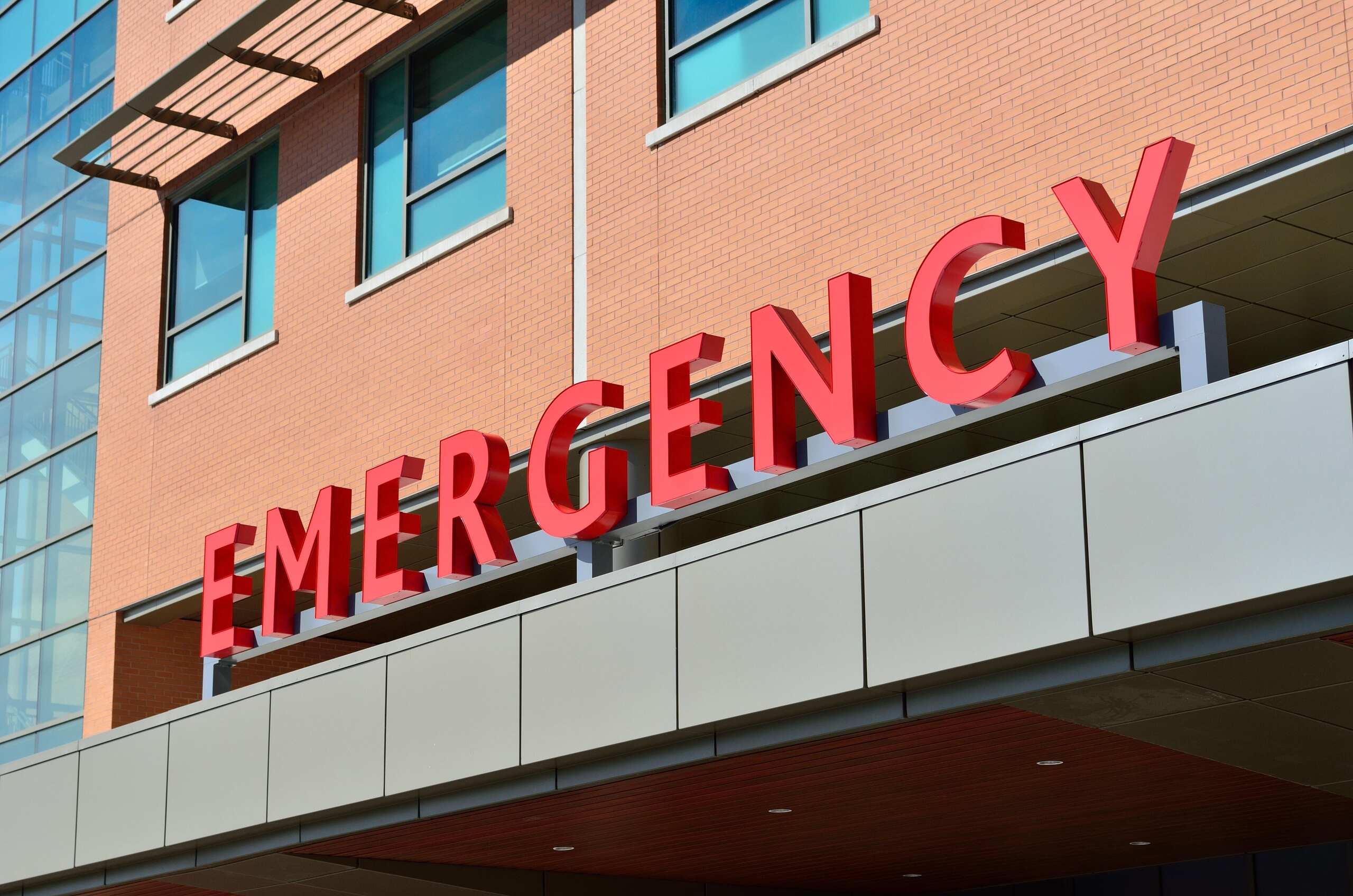 A large red "EMERGENCY" sign on the exterior of a brick hospital building, representing immediate trauma care evaluated by Scranton Amputation Injury Lawyers.