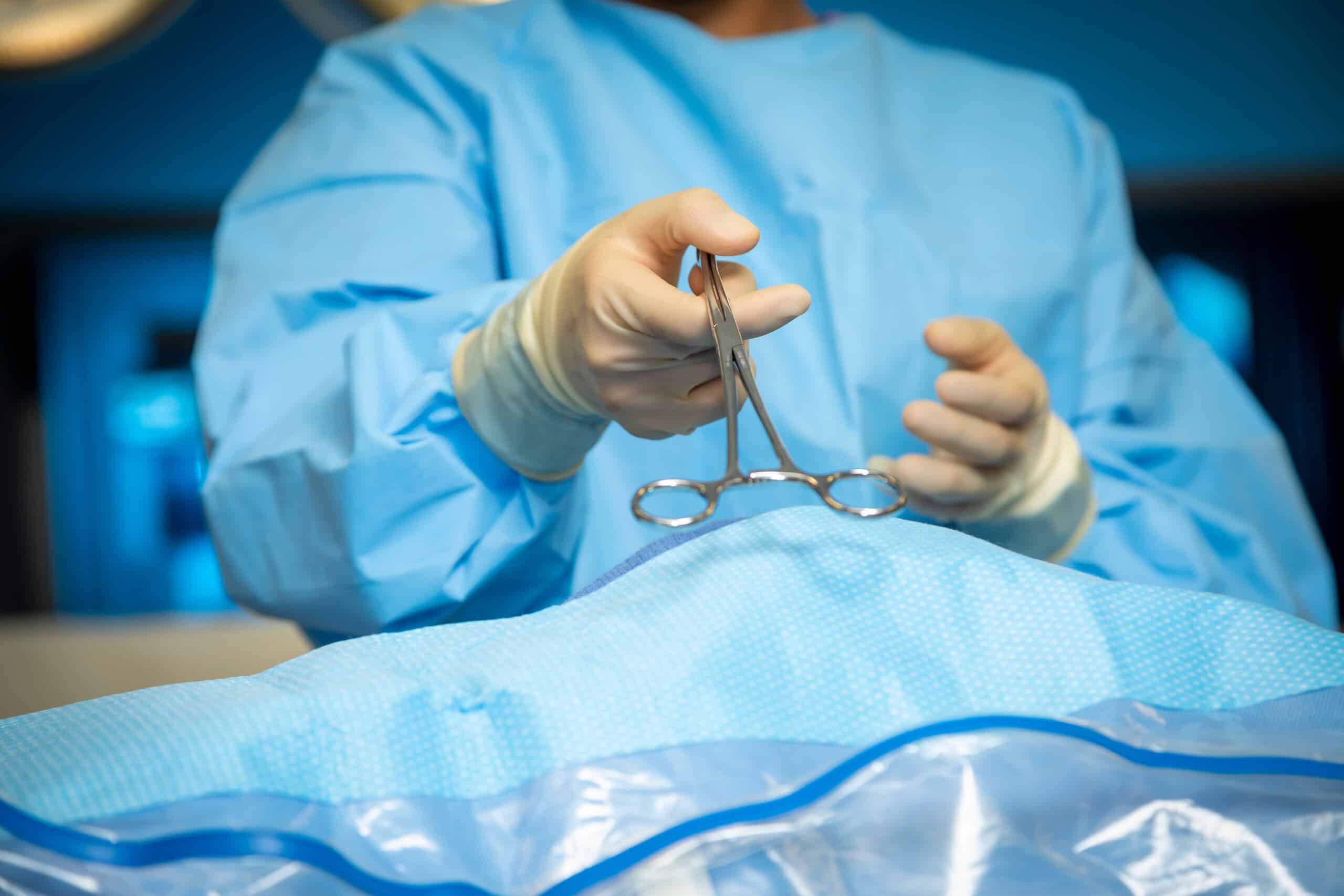 A surgeon in blue scrubs and sterile gloves holding surgical clamps over an operating table, illustrating medical treatment relevant to Scranton Amputation Injury Lawyers.