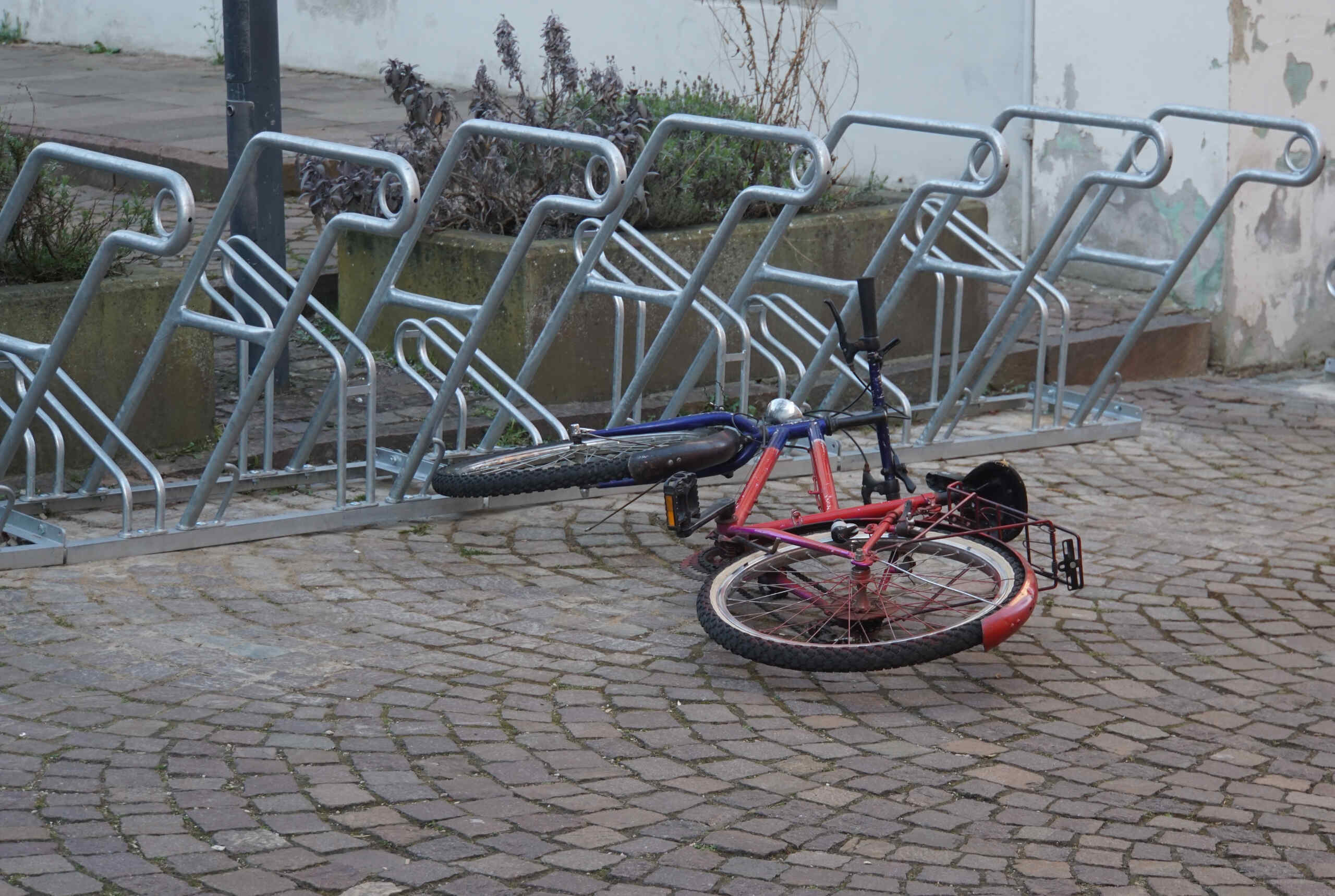 A multi-colored bicycle knocked over and lying flat on its side on a cobblestone pavement next to a metal bike rack, illustrating a collision claim handled by Scranton bicycle accident lawyers.