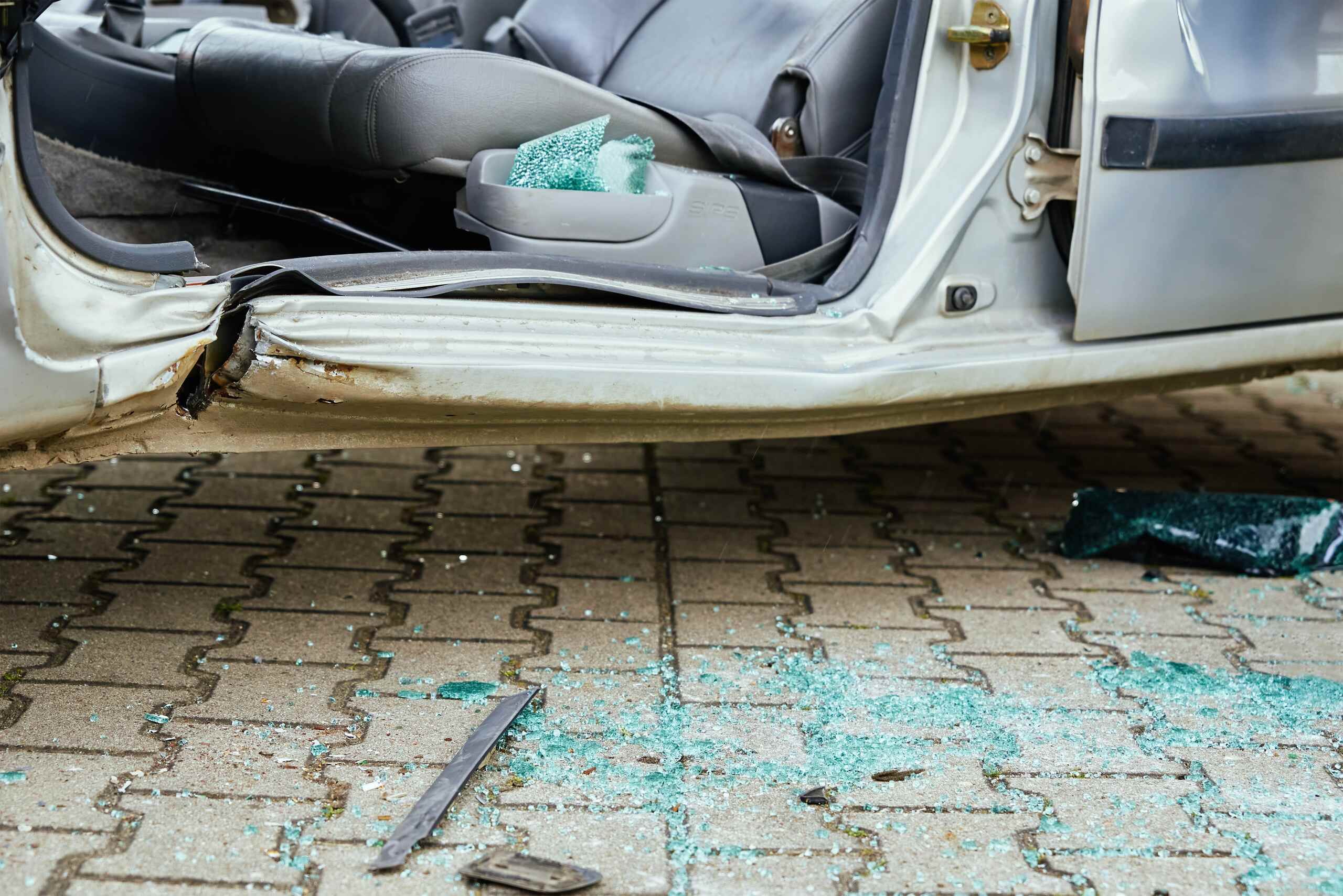 Shattered green window glass scattered on a paved ground next to a damaged open vehicle door, representing auto accident evidence for Scranton Catastrophic Injury Lawyers.