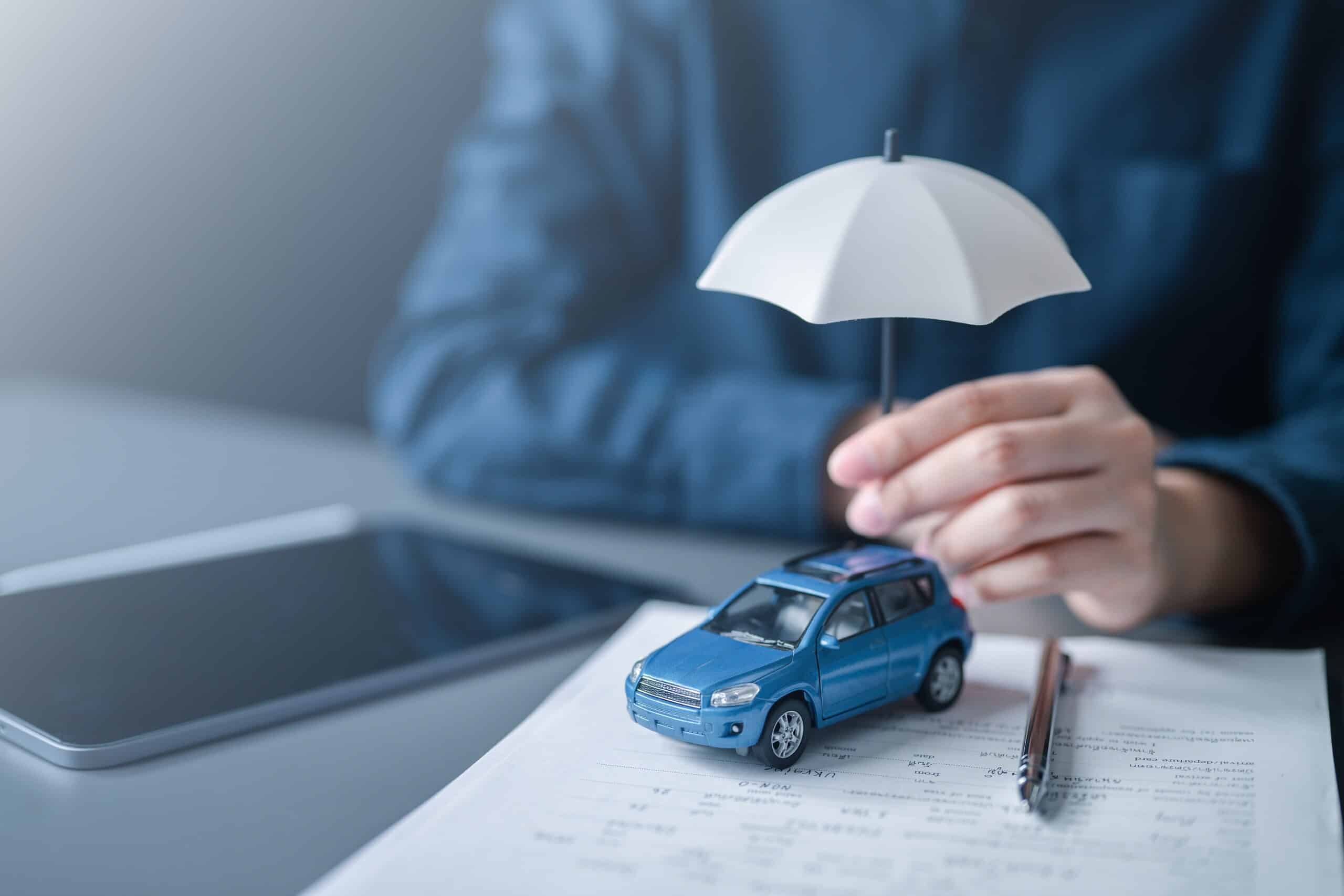 A person holding a small white umbrella over a blue toy car resting on legal paperwork, symbolizing accident insurance coverage pursued by Scranton Hit and Run Accident Lawyers.
