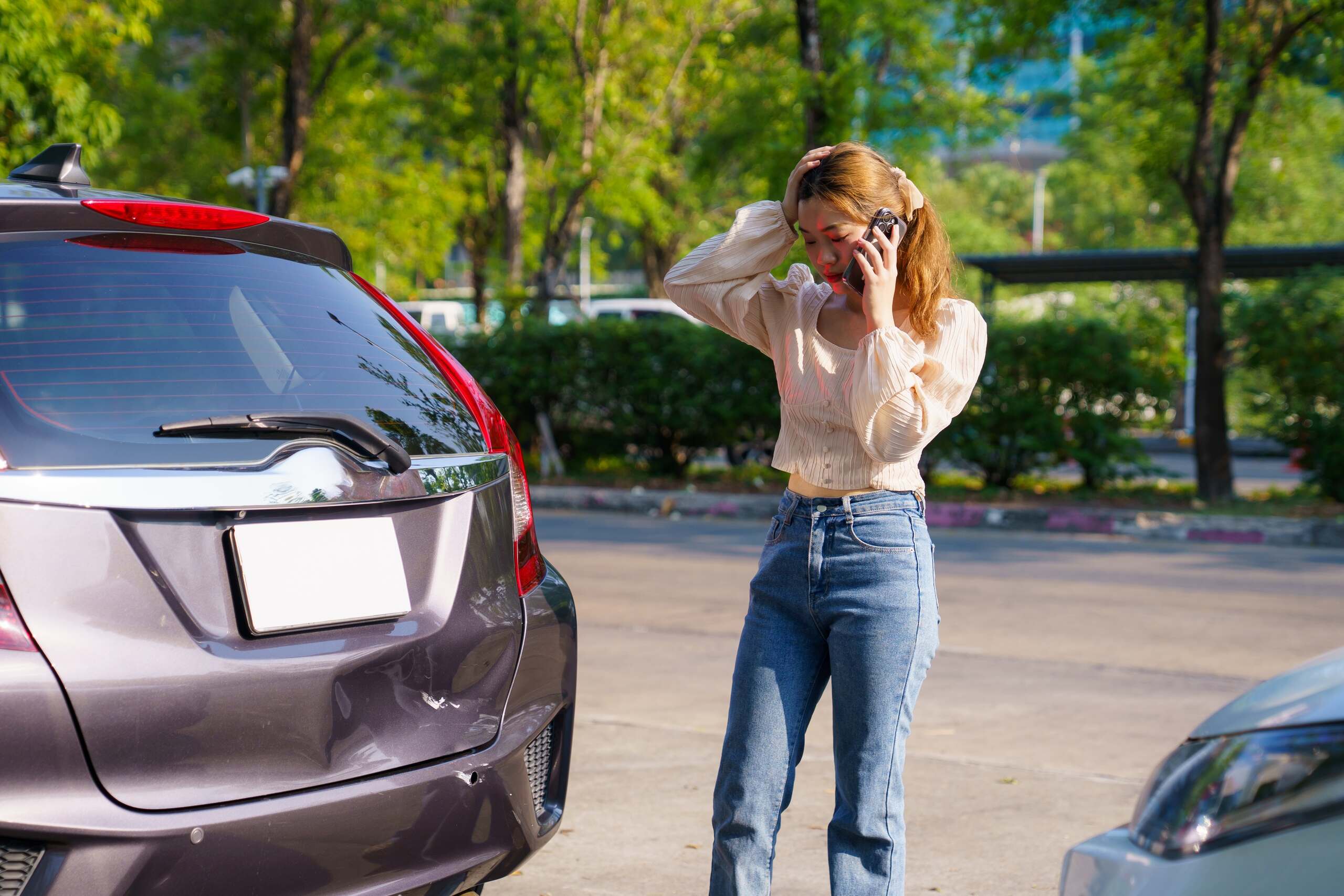 A stressed driver holding her head and calling for help next to a car with a dented rear bumper, illustrating an insurance claim handled by Scranton Uninsured Motorist Accident Lawyers.