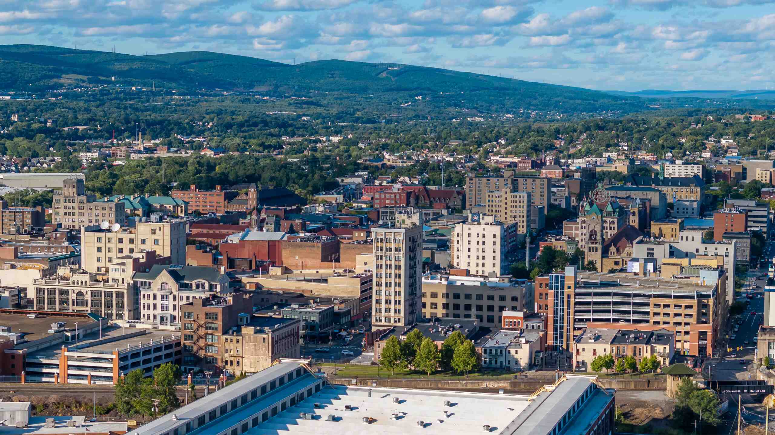High-angle aerial view of the Scranton, Pennsylvania city skyline with buildings and green mountains in the background, showing the area served by Scranton Workers’ Compensation Lawyers.