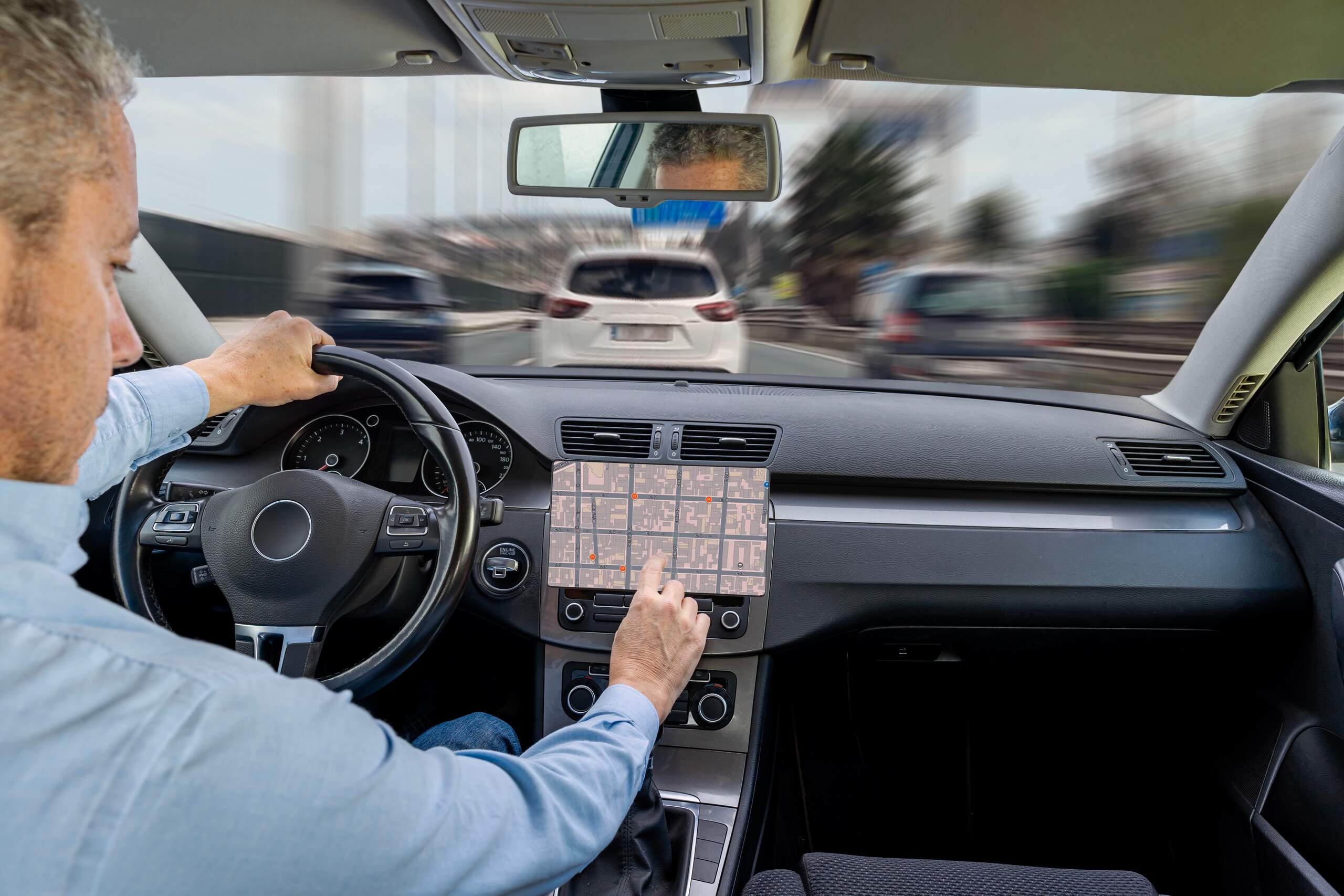 Driver touching a dashboard navigation screen while driving on a highway.
