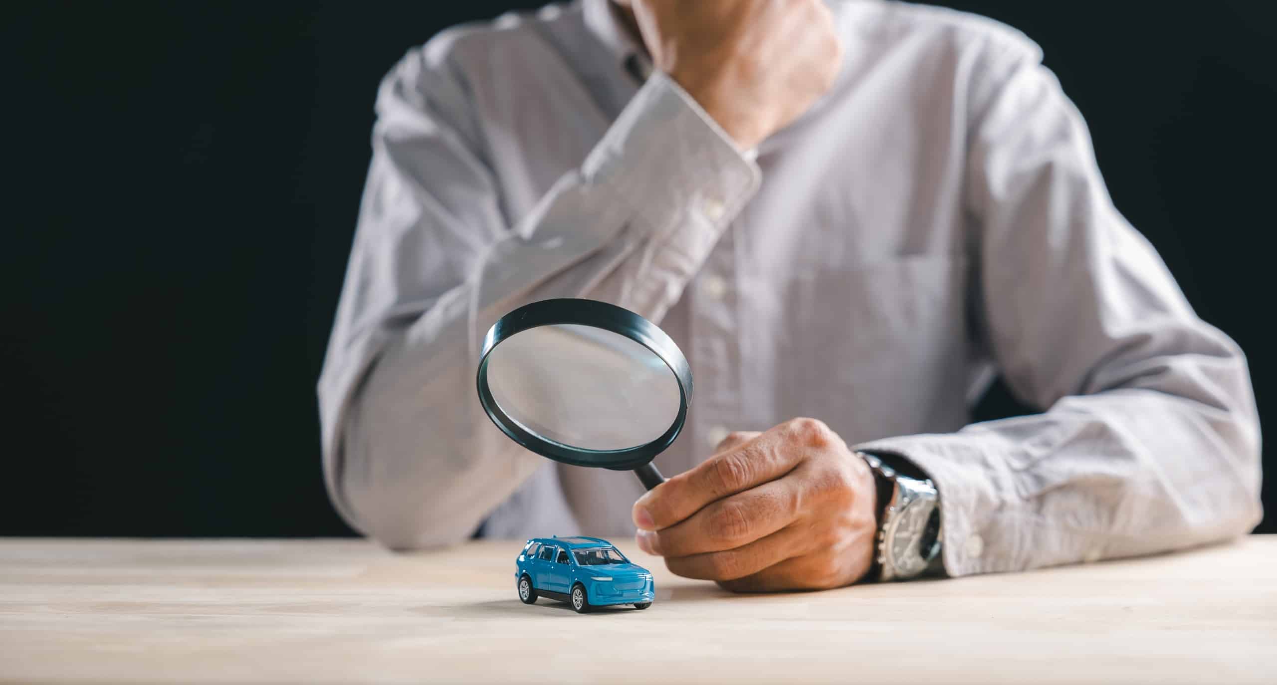 A person examining a toy car through a magnifying glass illustrates auto claims investigated by Pennsylvania Uninsured Motorist Lawyers.