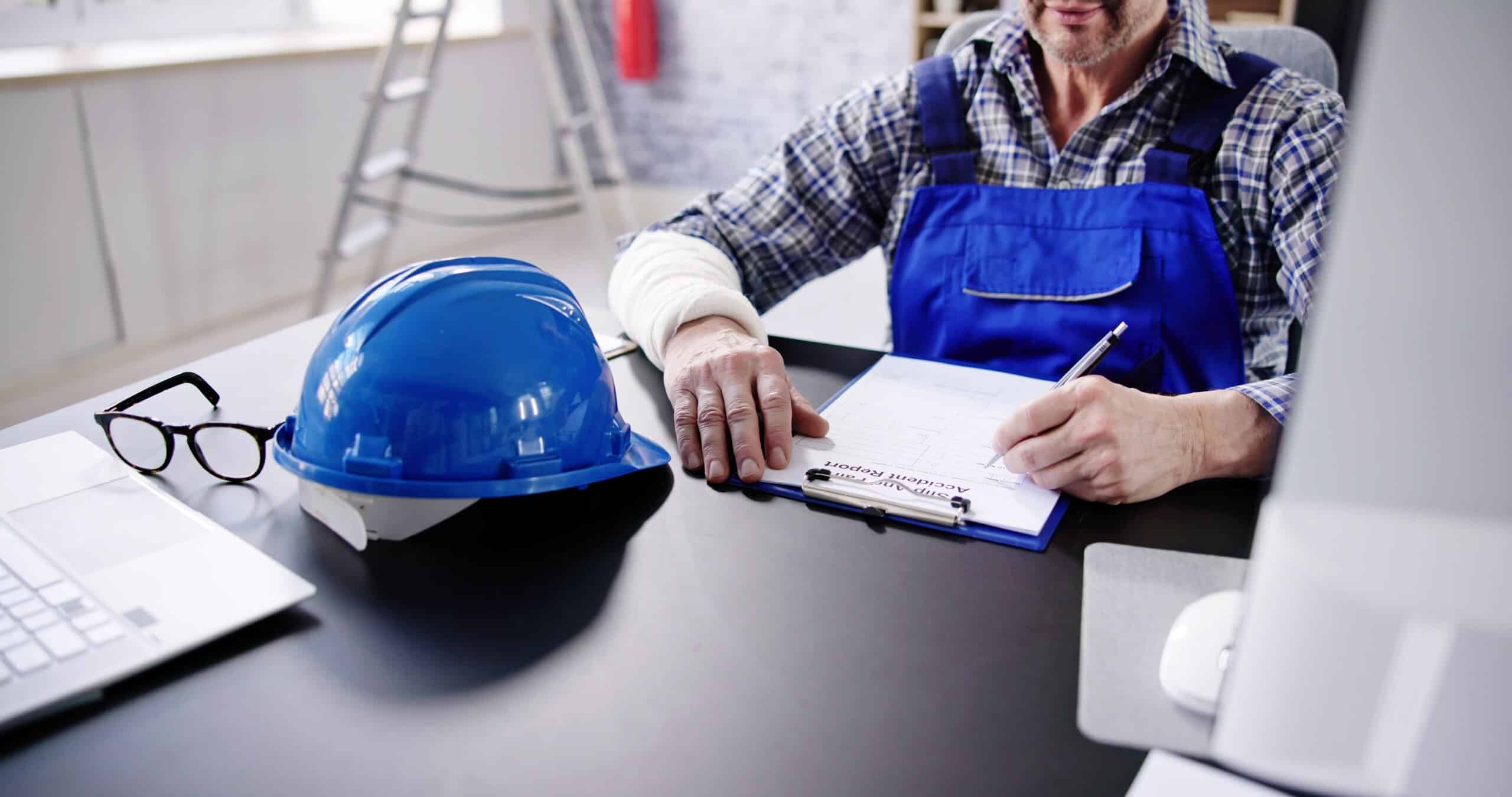 Injured worker filling out an accident report at a desk next to a hard hat.