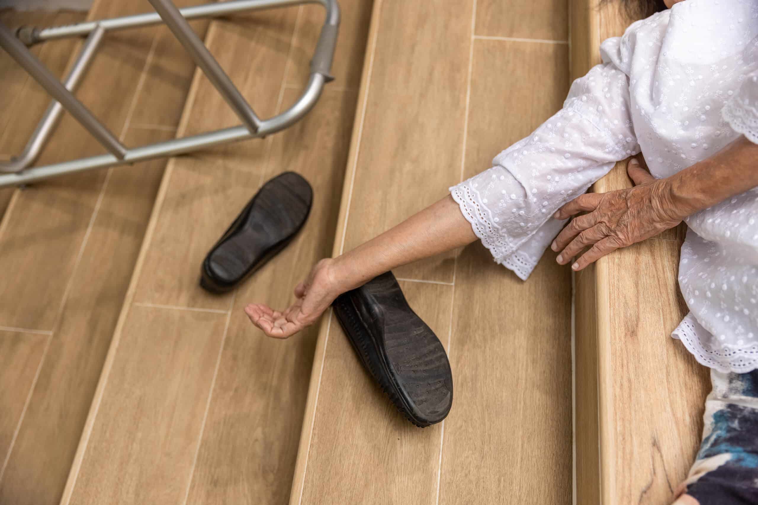Elderly person lying on wooden stairs next to a walker.