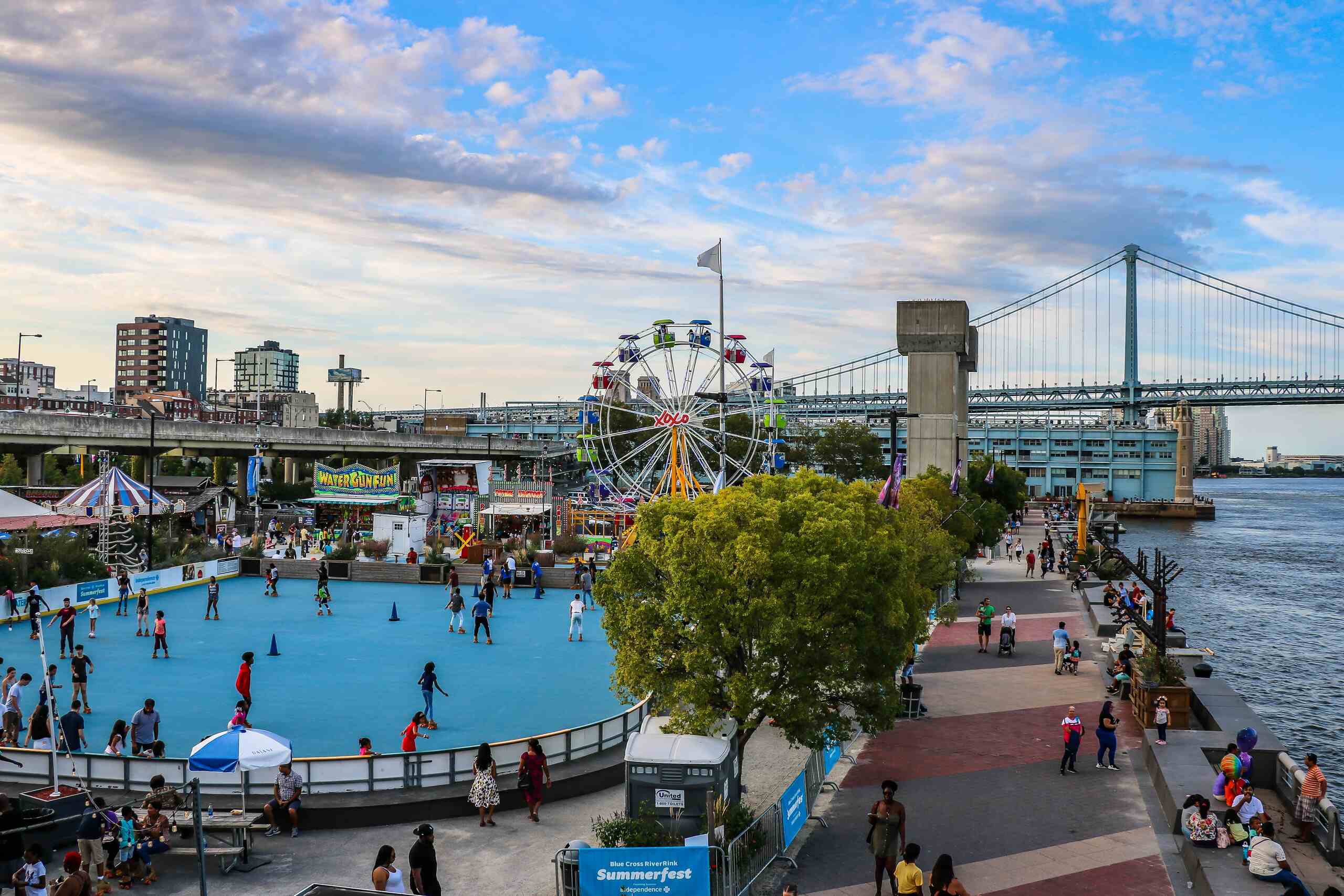 Penn's Landing boardwalk in Philadelphia with a Ferris wheel and Ben Franklin Bridge.