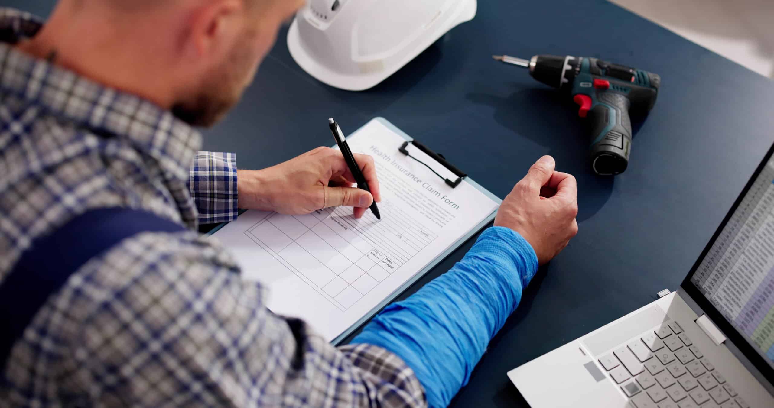Injured worker filling out a health insurance claim form at a desk.