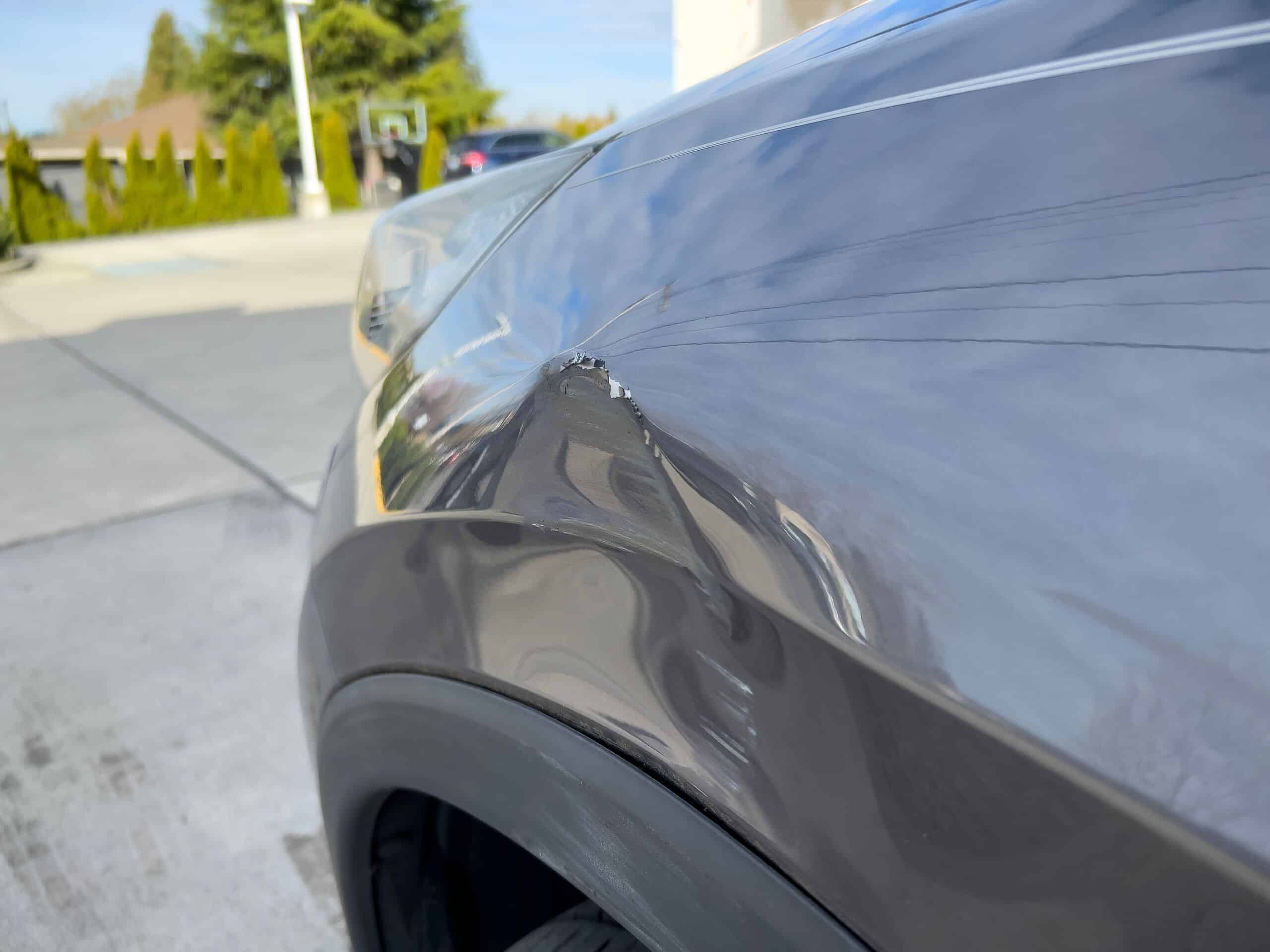 Close up view of a dent and scratch on a dark grey car fender.
