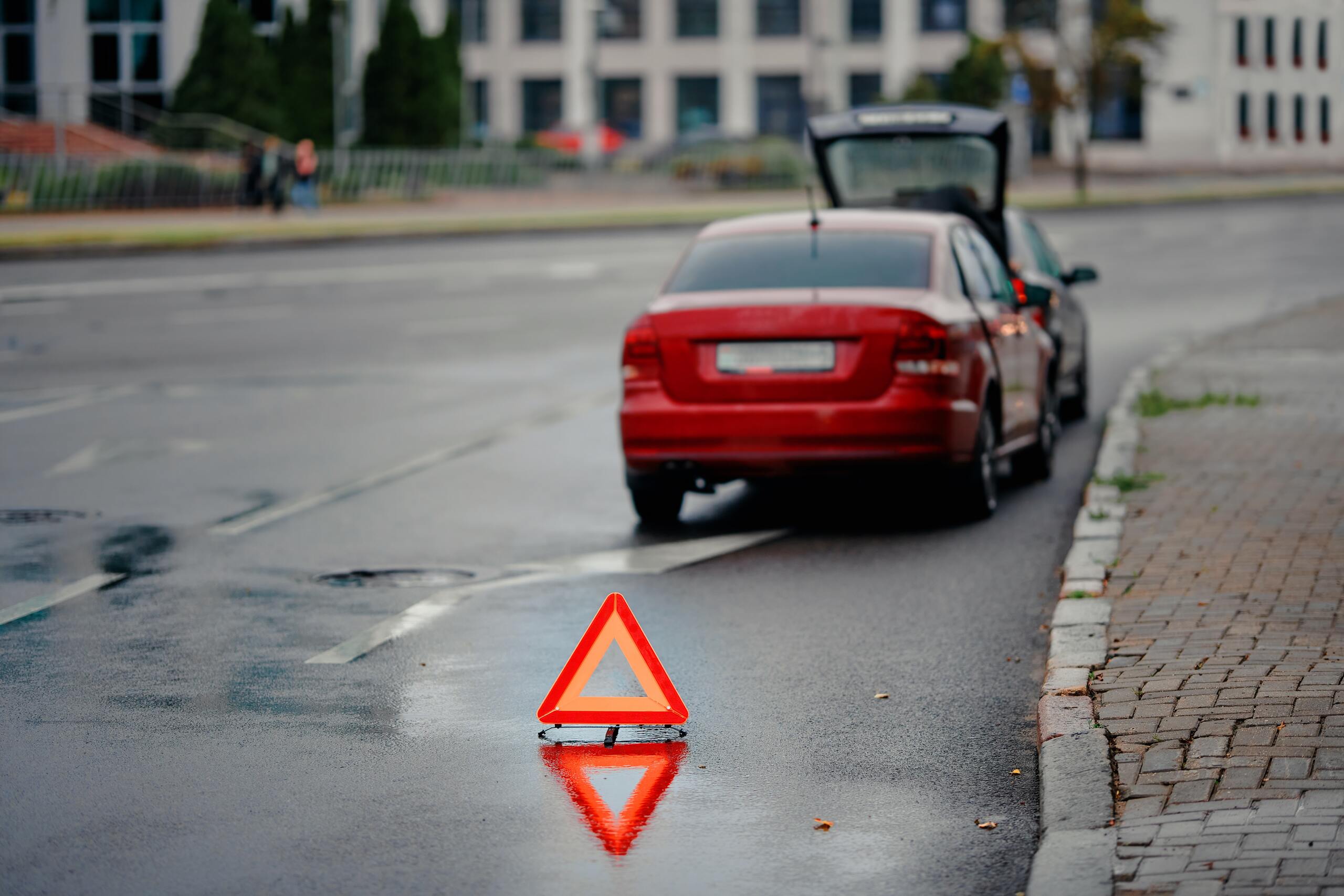 Emergency warning triangle placed on the street behind a broken down red car.