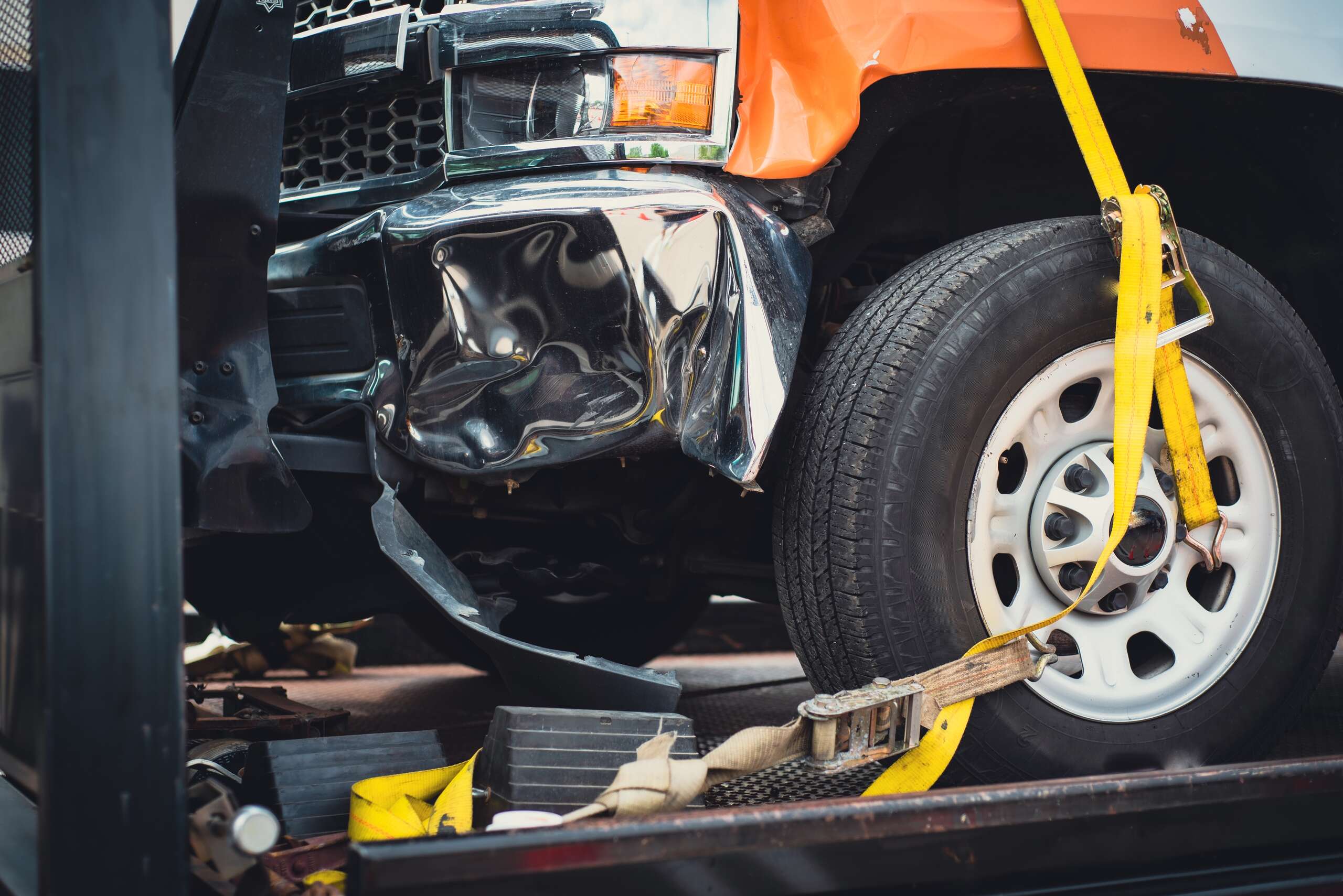 Damaged truck bumper secured onto a flatbed trailer with yellow straps.